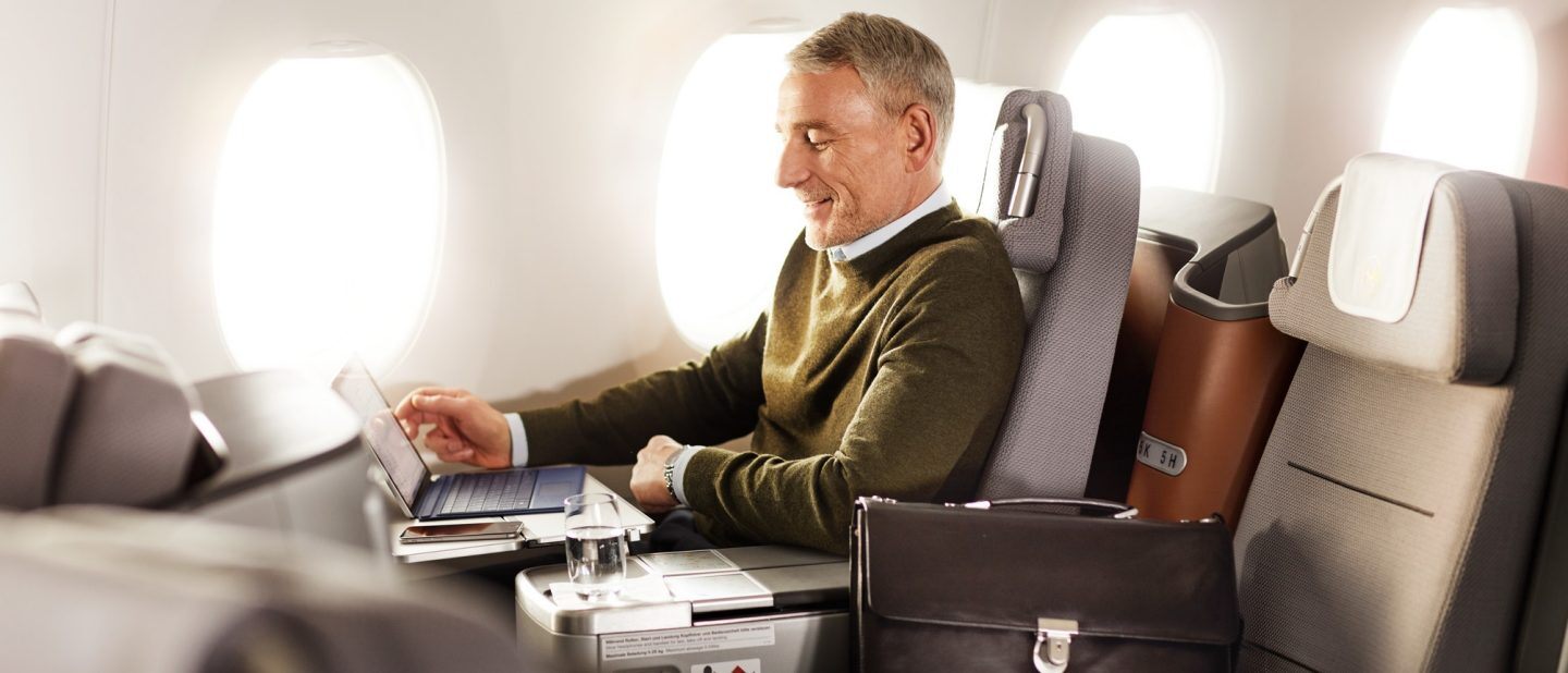 A man works on his laptop while in his Lufthansa Business Class seat, which can be enjoyed with a cheap flight with Flight Centre.