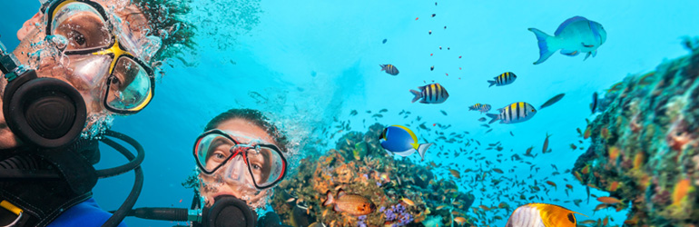 A couple scuba dive in the Maldives, which can be visited with a holiday package from Flight Centre.