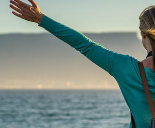 A woman stands with her arms stretched on the beach with a view of Table Mountain in Cape Town, which can be visited with a cheap holiday package from Flight Centre.