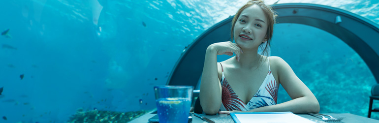 A woman sits at a table at an underwater restaurant in the Maldives, which can be visited with a holiday package from Flight Centre.